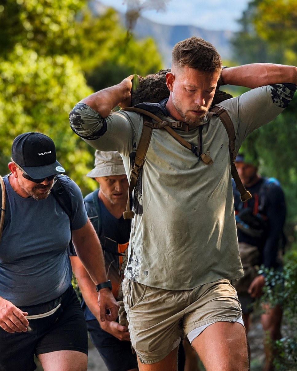 Jonny carrying a weighted load uphill on a trail with a group behind him